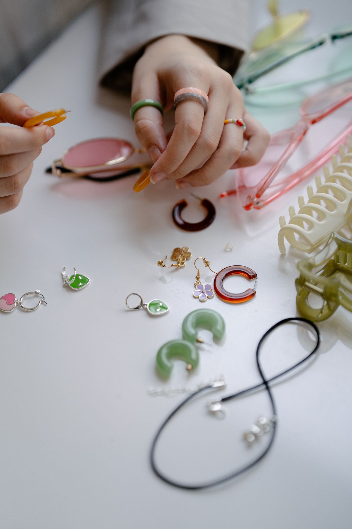 Hands arranging colorful jewelry and accessories on a white surface, ideal for craft enthusiasts.