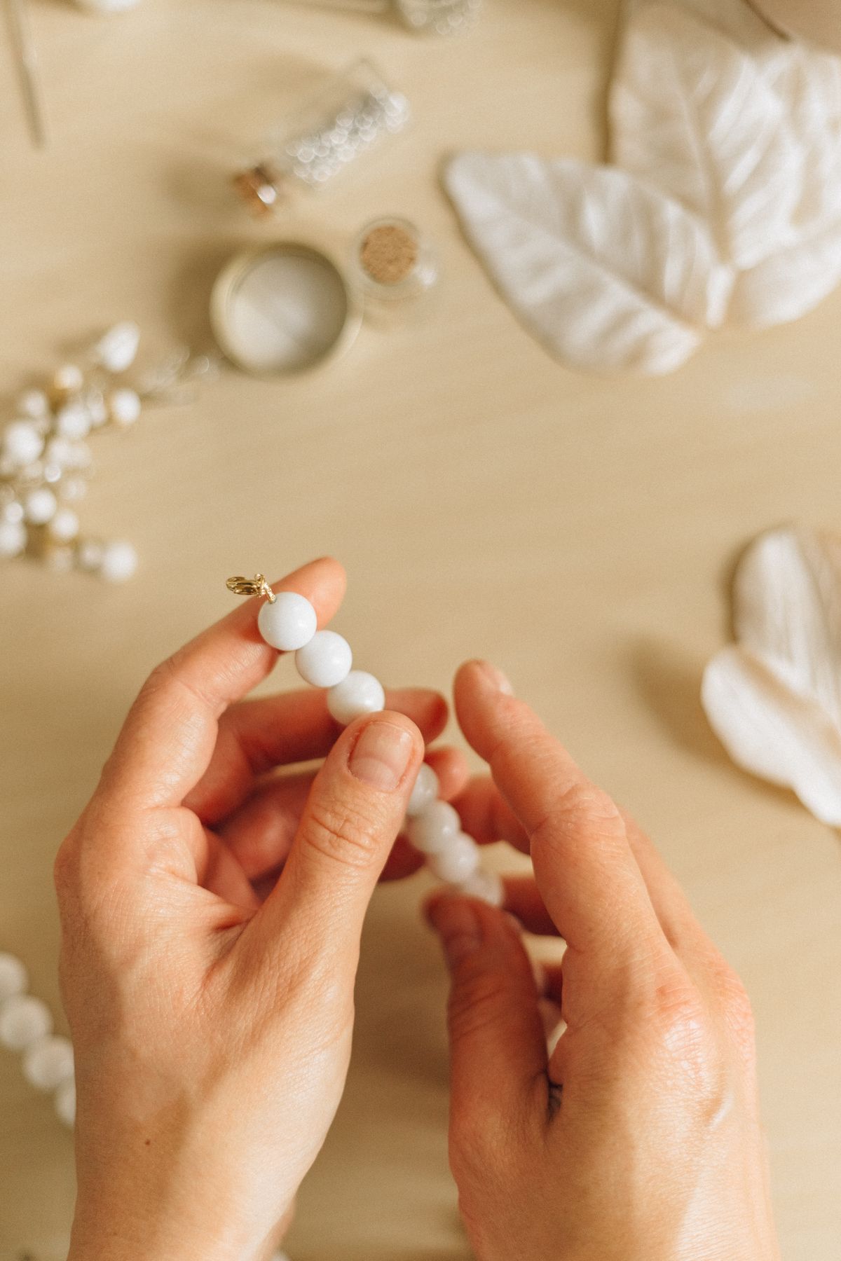Close-up of hands crafting handmade bead necklace on a wooden surface.